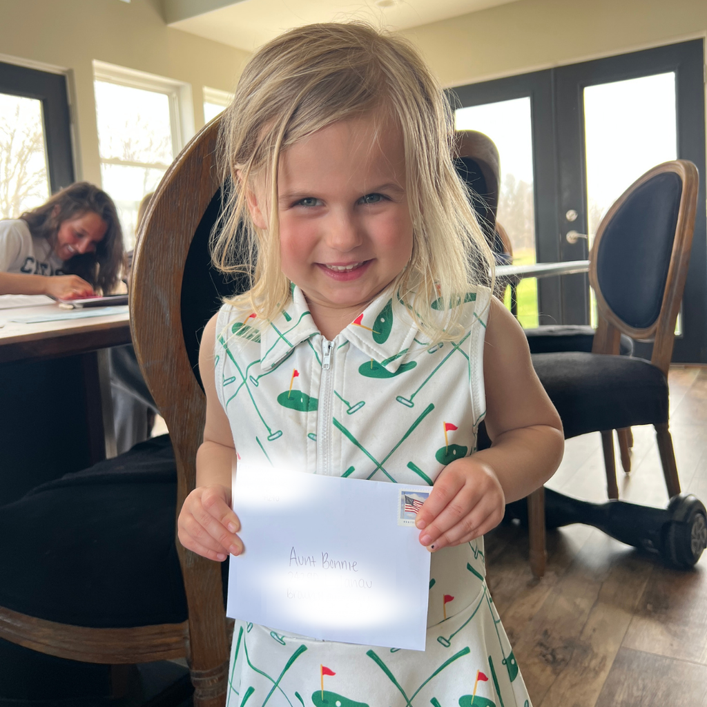 Young girl in a patterned dress holding a piece of paper indoors.